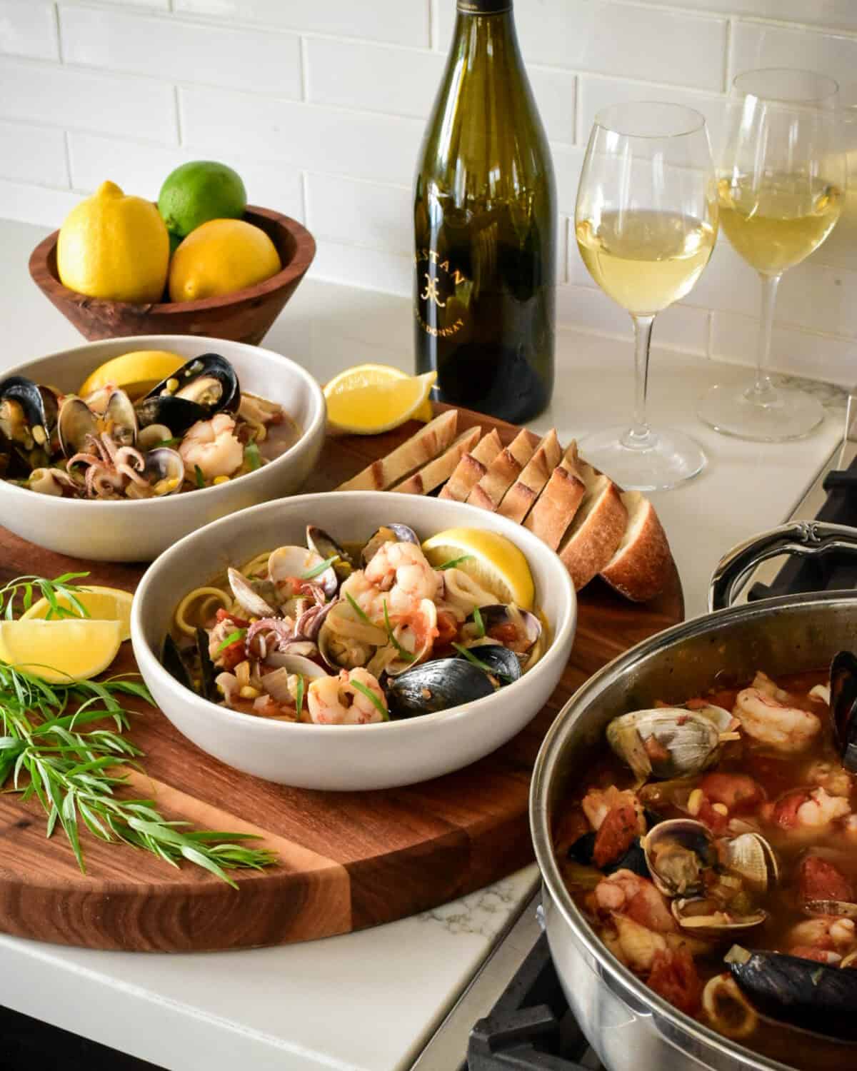 A pot and two bowls of Cioppino served with linguine , tarragon, lemons and bread.