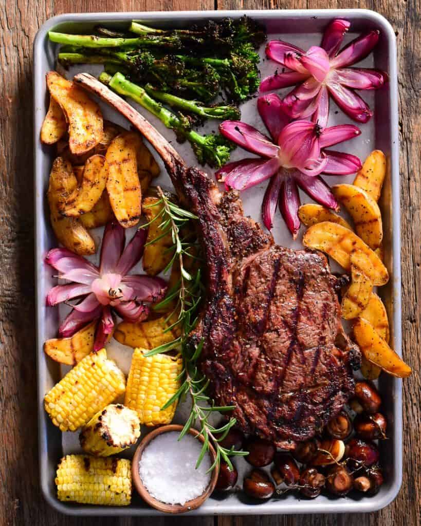 A bone in ribeye tomahawk steak with roasted red onion flowers.