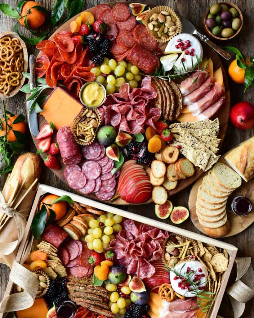 Two large charcuterie boards with a variety of meats, cheeses and vegetables.