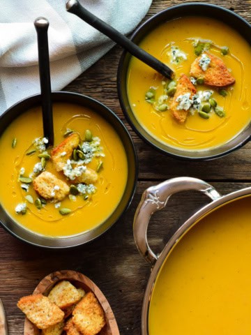 Two bowls and a pot of puréed roasted vegetable soup.