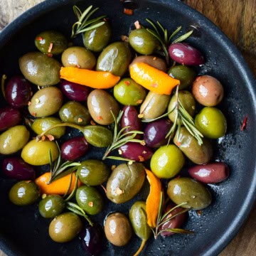 A skillet of warm olives with rosemary and clementine peels.