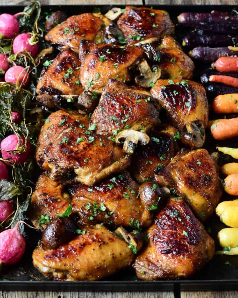At top down image of glazed and roasted Chicken Thighs with mushrooms and vegetables on the side.