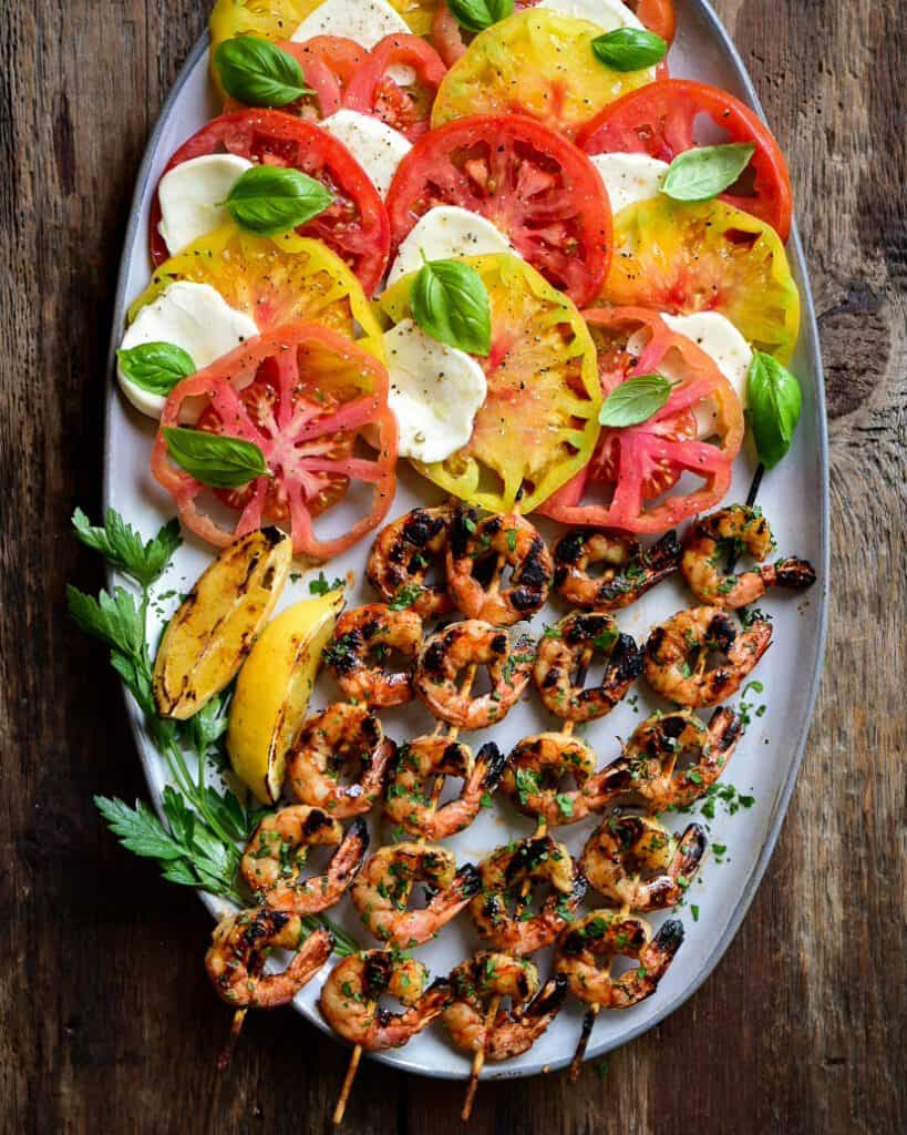 Four sweet and spicy grilled shrimp skewers served with a Caprese salad.