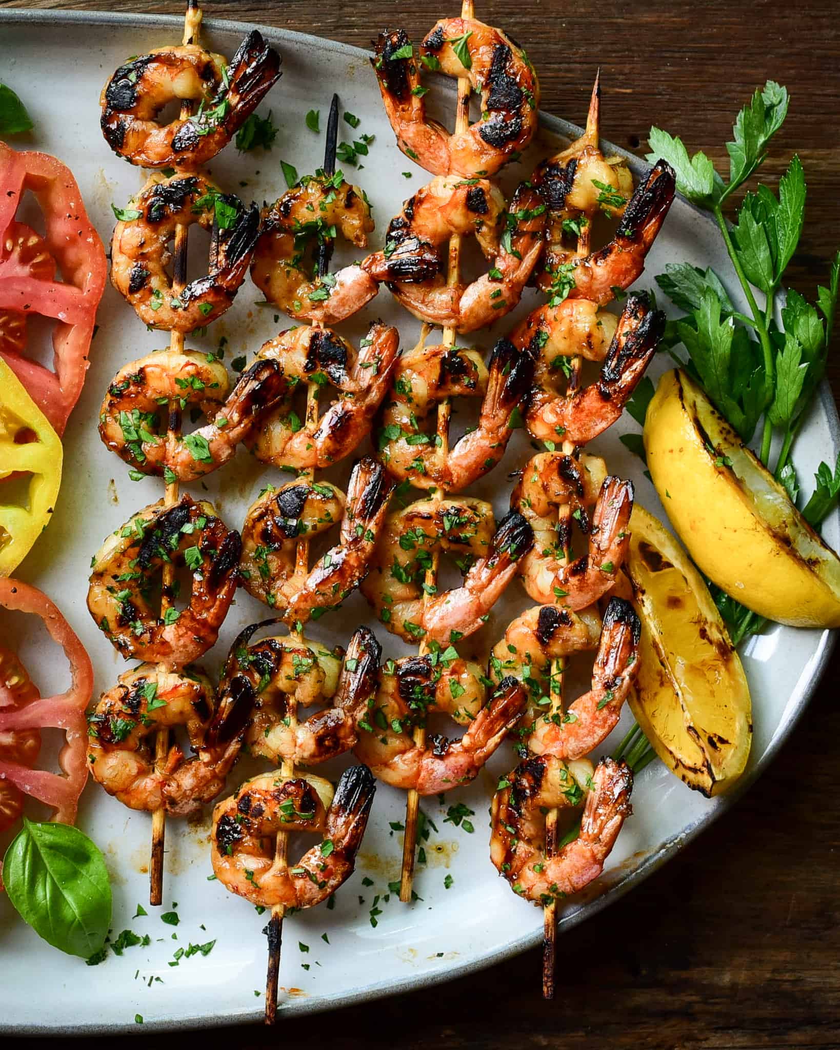 Four skewers of grilled shrimp served with grilled lemons and a tomato salad.