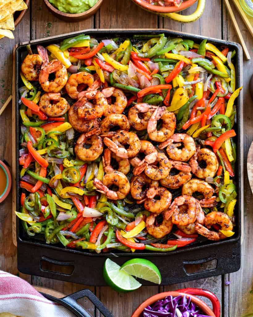 A square cast-iron skillet with fajita shrimp and vegetables.
