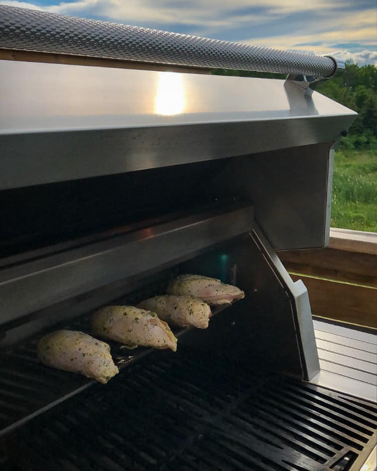 Four chicken breasts on the top rack of a grill.