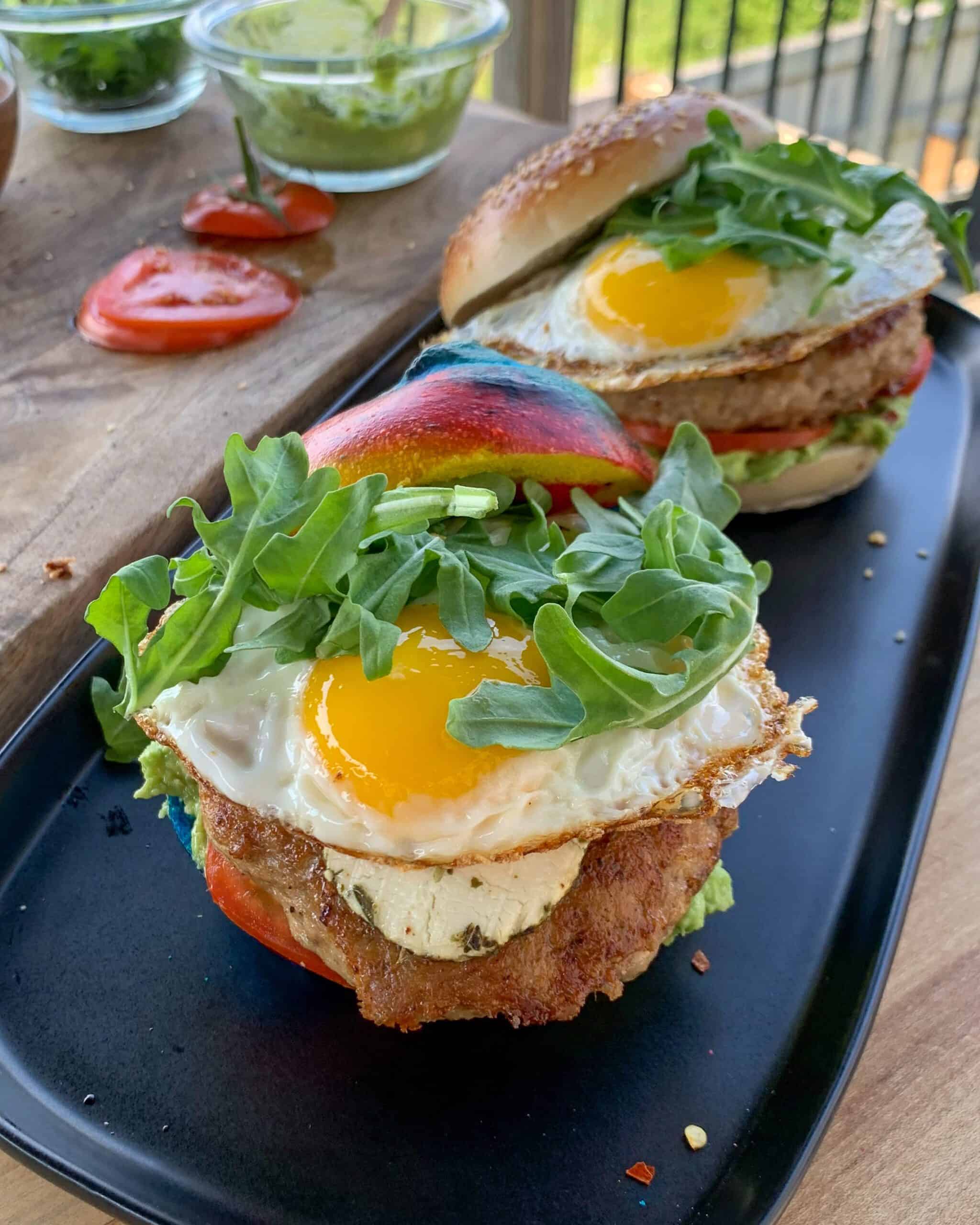 Two rainbow bagels breakfast burger with a sunny side up fried egg.