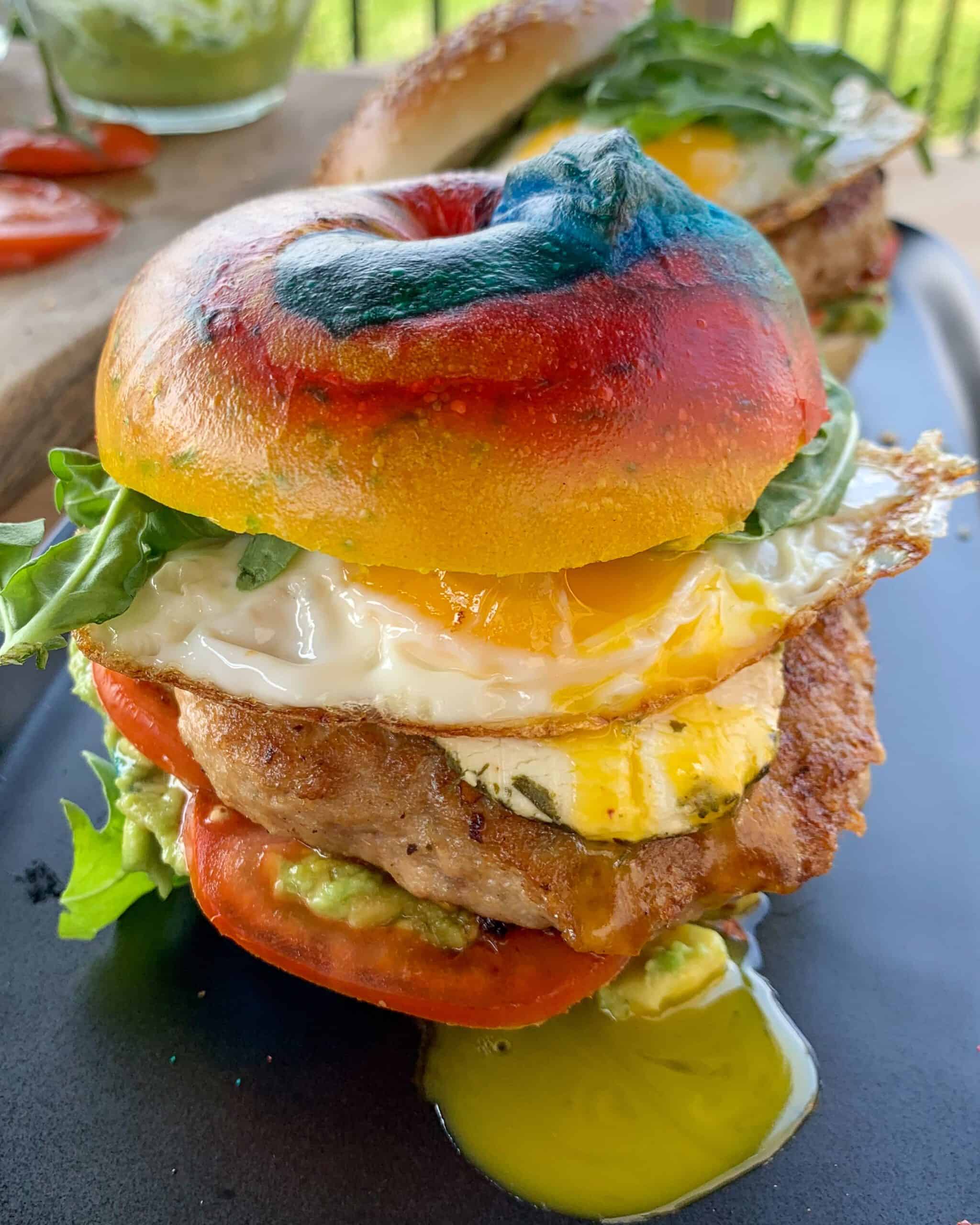 A rainbow bagel breakfast burger with a dripping yolk.