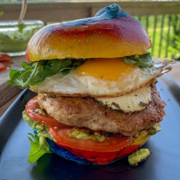 A stacked rainbow bagel breakfast burger with a fried egg.