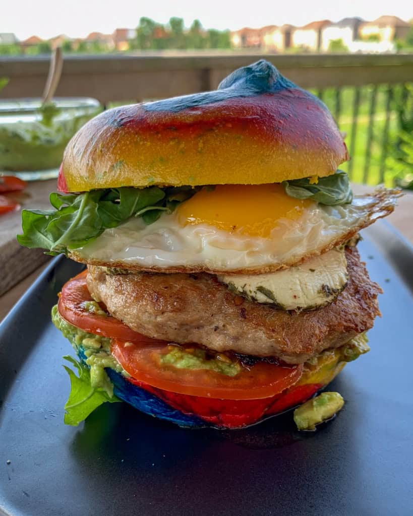 A stacked rainbow bagel breakfast burger with a fried egg.