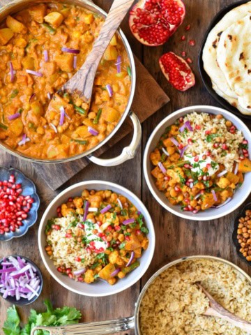 A pot of Roasted Butternut Squash, Cauliflower & Chickpea Curry with two bowls and toppings.