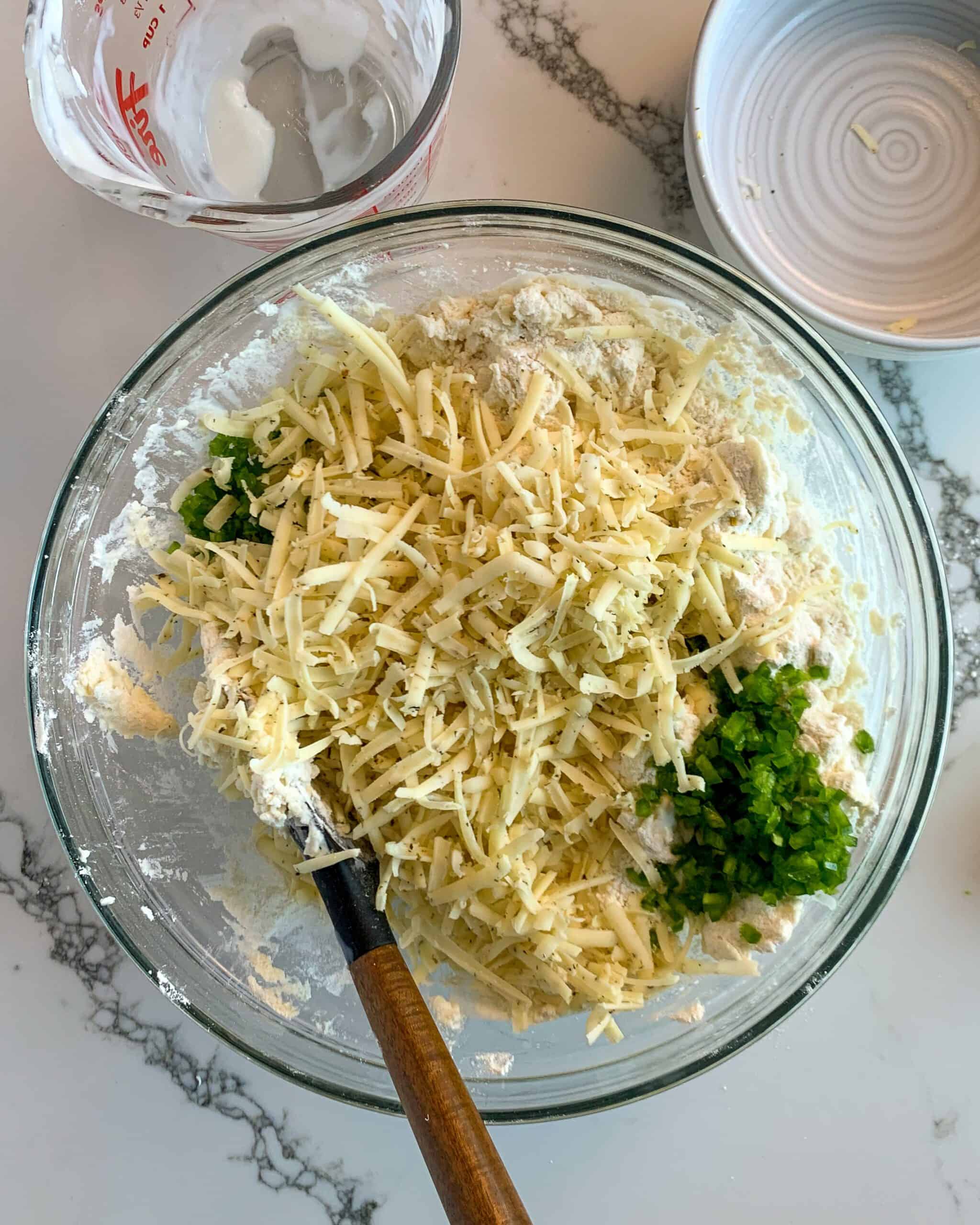 A mixing bowl with dry ingredients with shredded cheese and jalapenos added in.