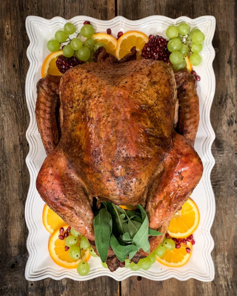 Roasted Turkey on a rectangular platter. Garnished with grapes, oranges and pomegranates.