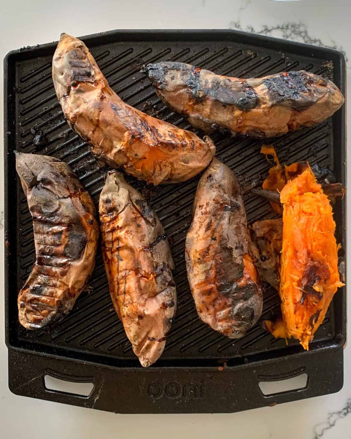 Six baked sweet potatoes with the skin peeled off on one.
