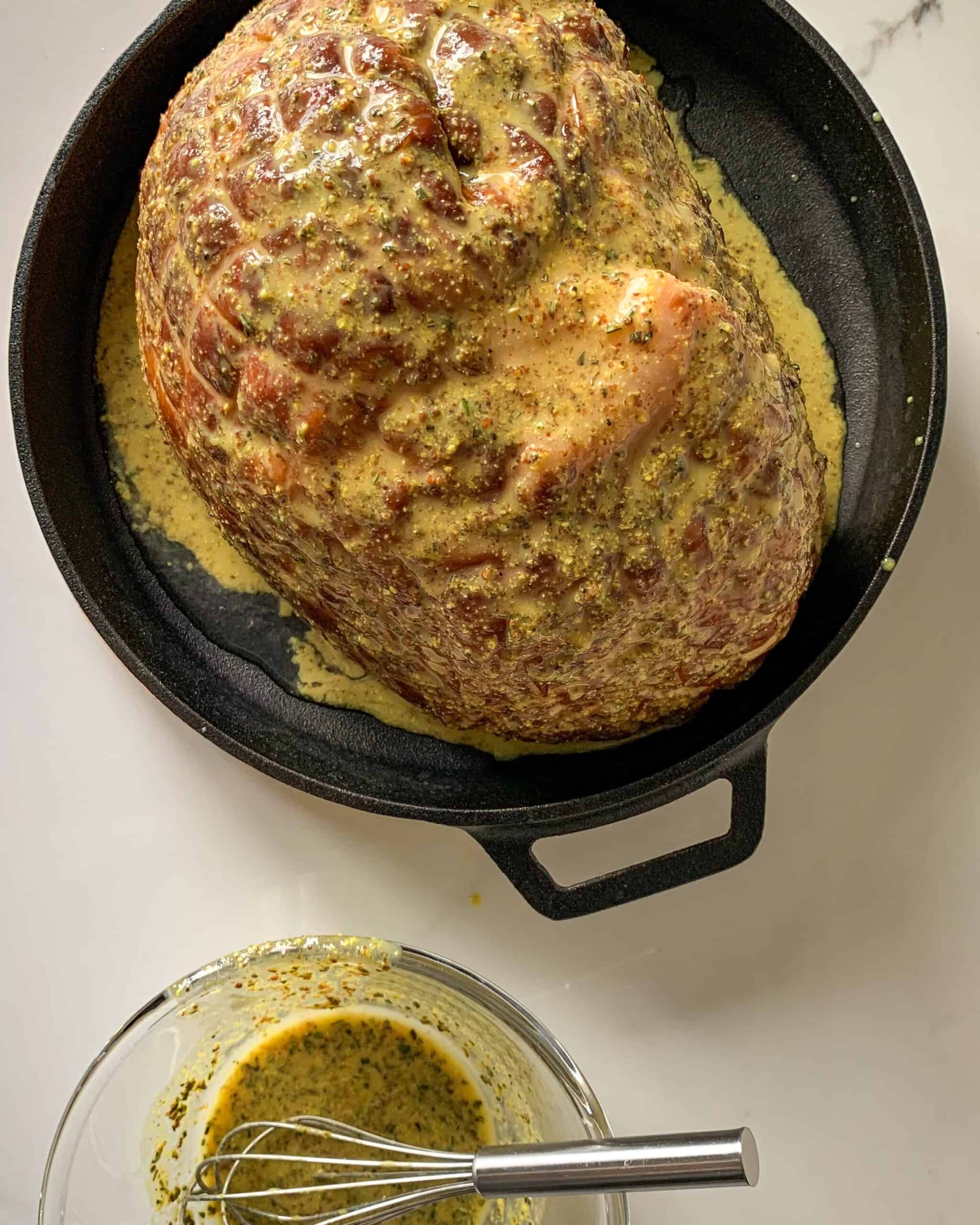 An image of a ham in a round cast iron pan with sauce on it and in a bowl beside the pan.