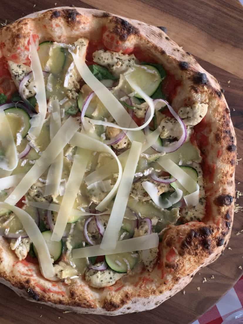 A top down image of a lemon-rosemary chicken pizza topped with strips of Comte cheese.
