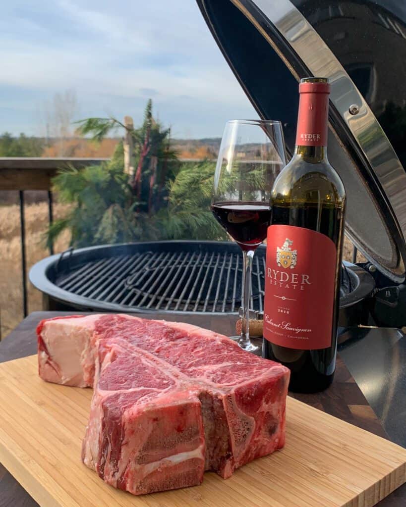 A beautiful 2 ½ inch steak sitting on a cutting board about to go on the bbq beside a bottle and glass of wine.