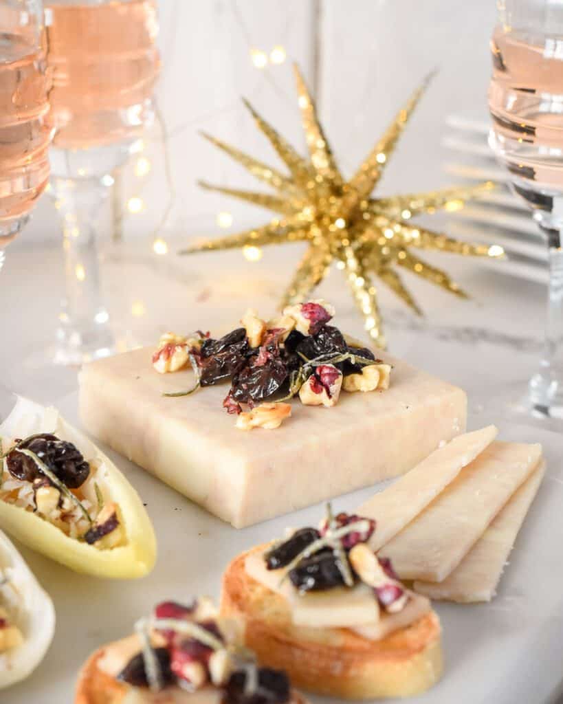 A block of cheese with a pile of walnuts, dried cherries and rosemary on top with a sparkly star in the backdrop.