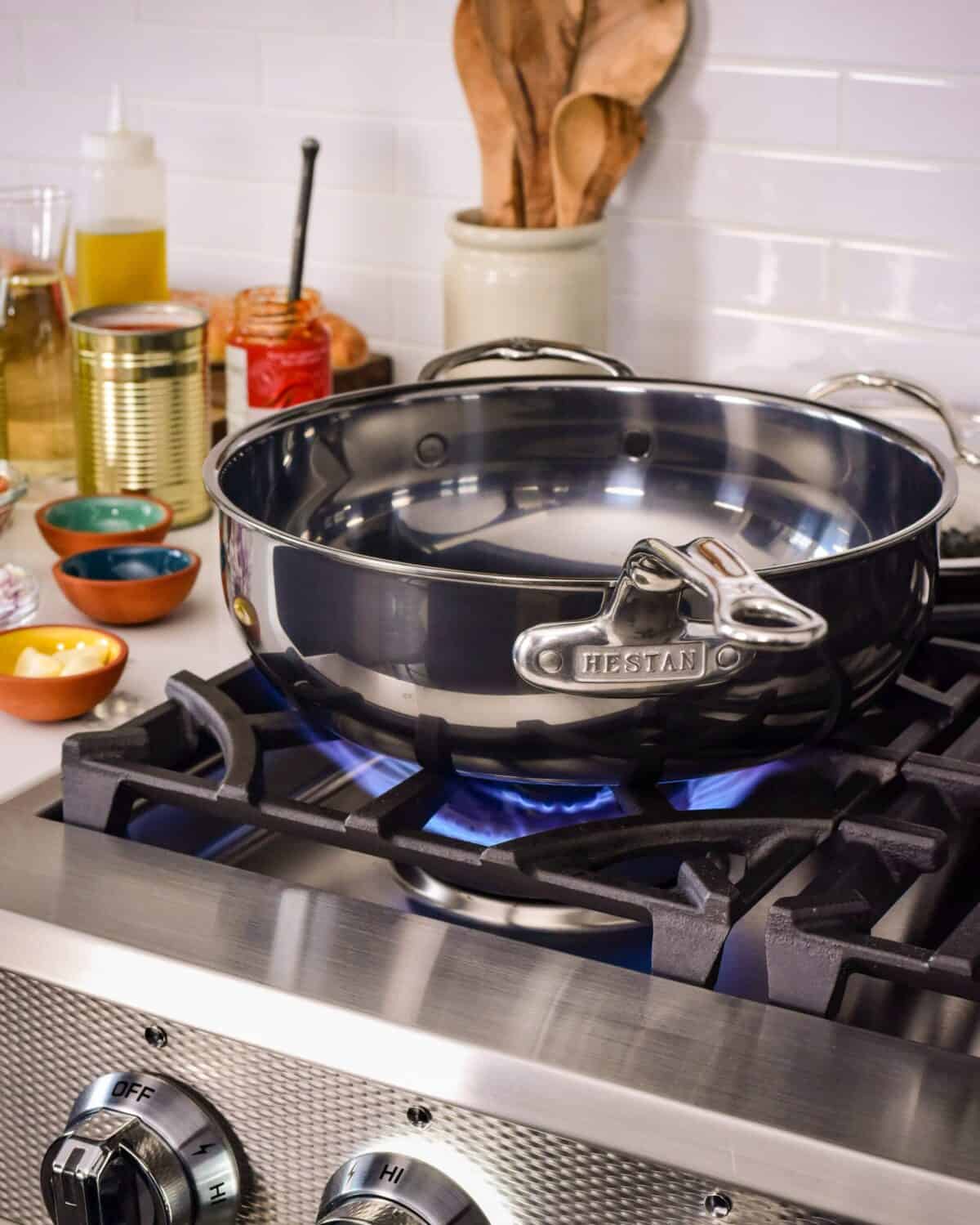 An image of an large pan on a gas range being heated up. Ingredients are on the counter beside the range.
