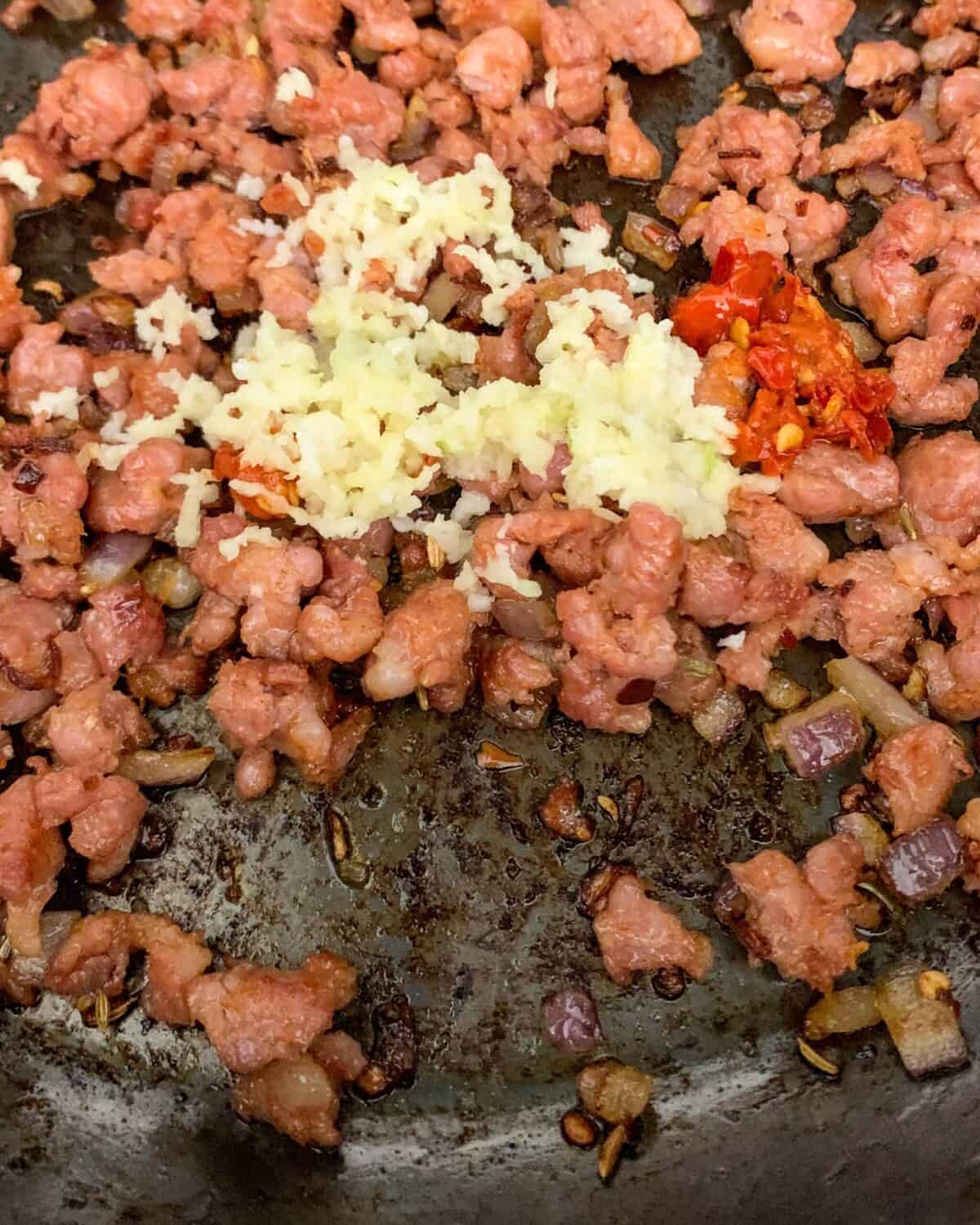 An image of browning the sausage and other ingredients for a mussels with sausage recipe.