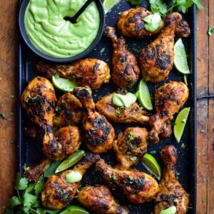 A platter of charred chicken drumsticks with a bowl of Peruvian sauce and limes.