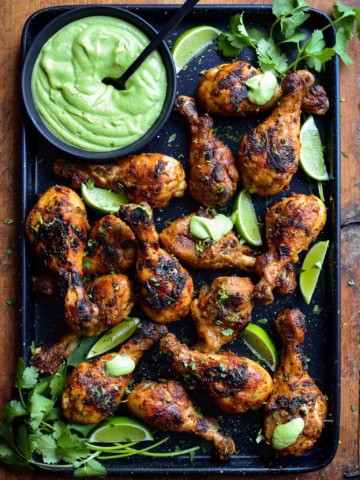 A platter of charred chicken drumsticks with a bowl of Peruvian sauce and limes.