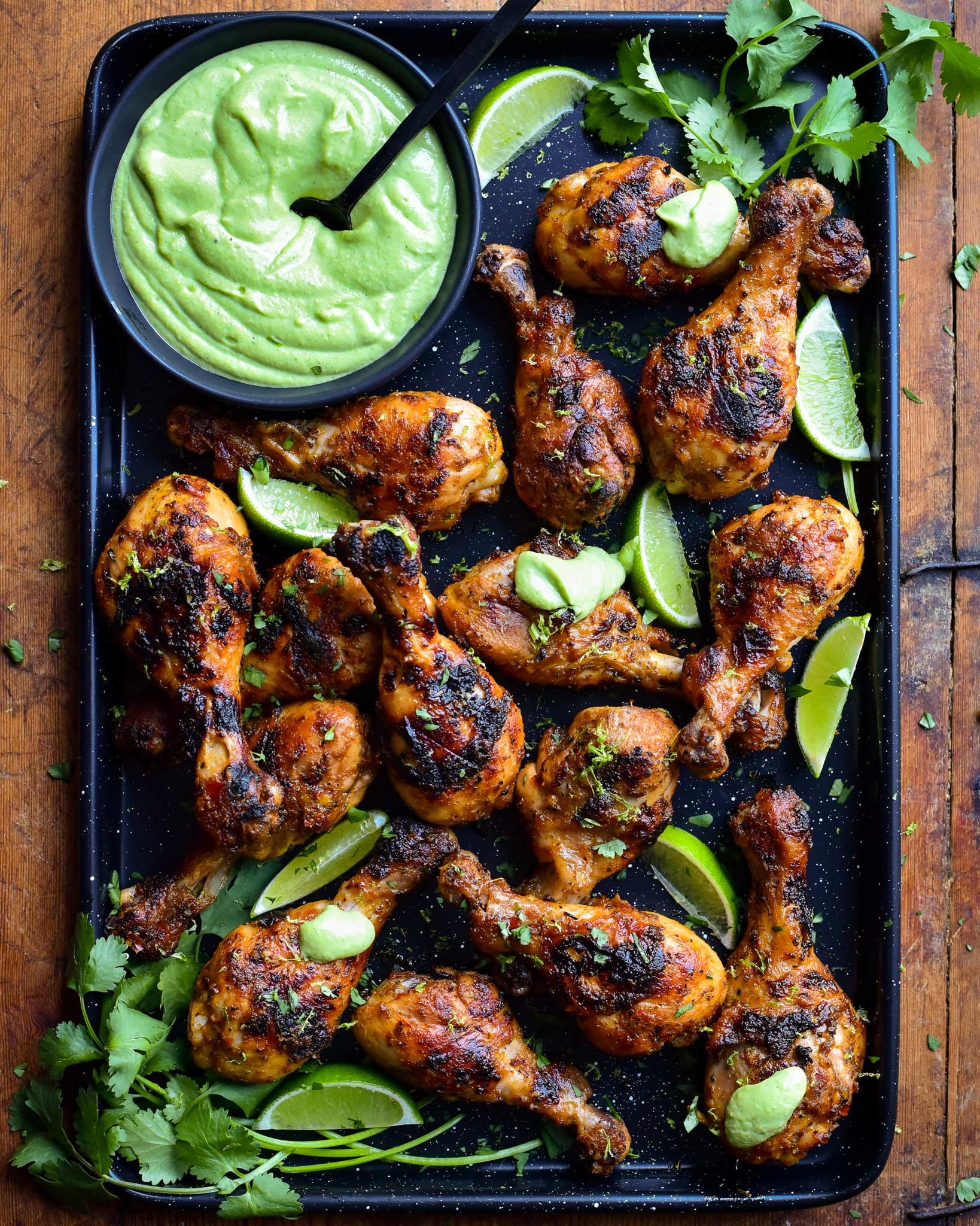 A platter of charred chicken drumsticks with a bowl of Peruvian sauce and limes.