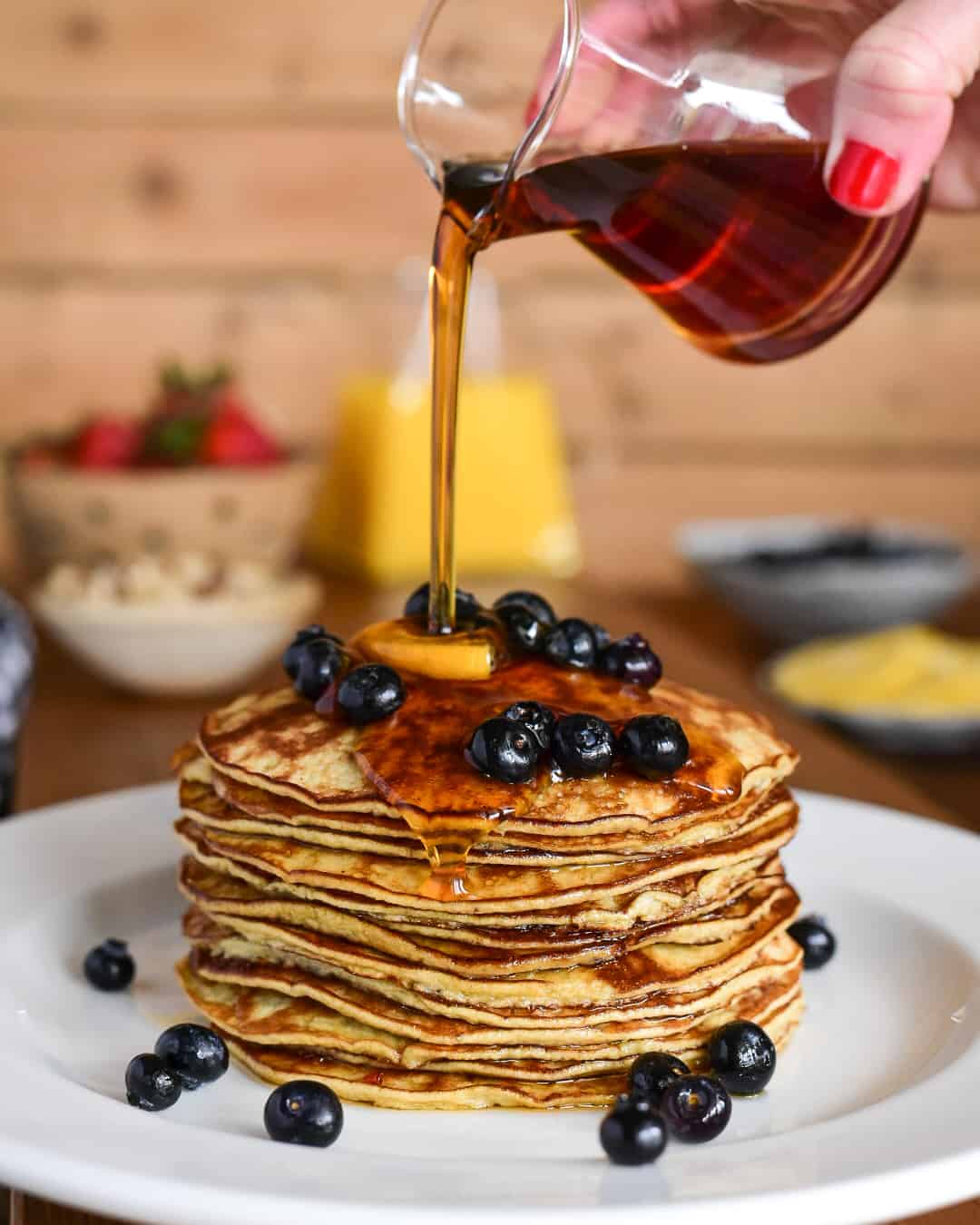 Two Ingredient Banana Pancakes - stack with blueberries and lemon and a stream of pouring syrup.