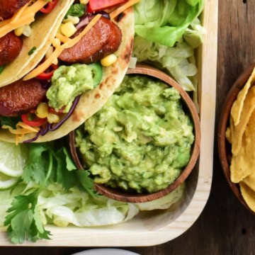 A bowl of spicy guacamole on a platter of tacos