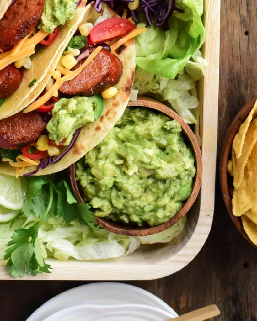 A bowl of spicy guacamole on a platter of tacos