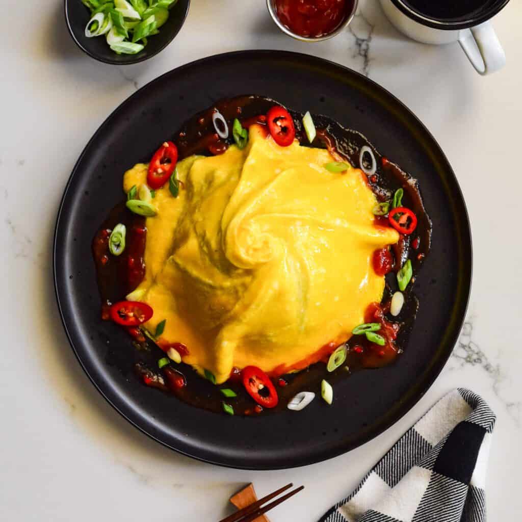 A domed and swirled omelette over a pile of rice (not shown) with sauce and toppings around the base.