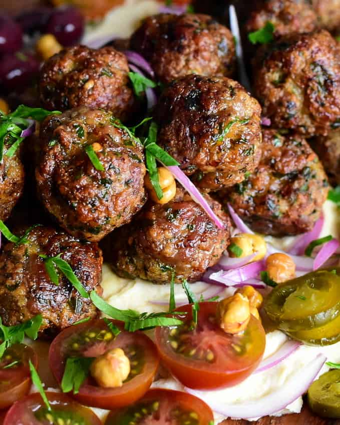A close up of sausage balls on a loaded hummus platter.