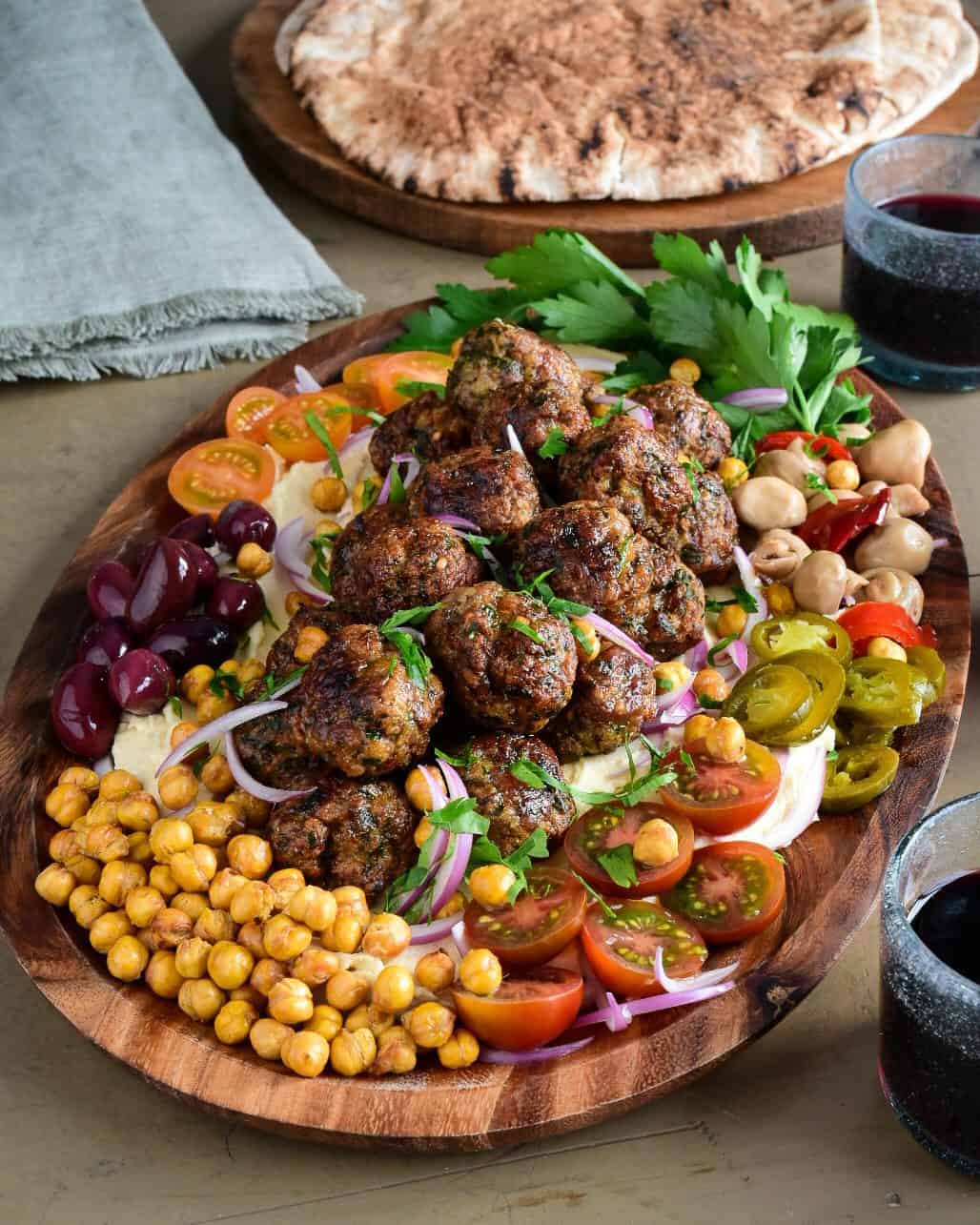 A platter of Loaded Hummus with Air Fryer Harissa Sausage Balls with a selection of fresh and pickled vegetables and herbs.