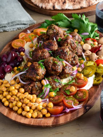 A platter of Loaded Hummus with Air Fryer Harissa Sausage Balls with a selection of fresh and pickled vegetables and herbs.