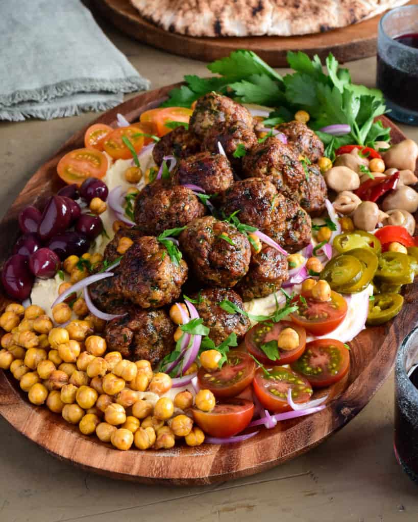 A platter of Loaded Hummus with Air Fryer Harissa Sausage Balls with a selection of fresh and pickled vegetables and herbs. 