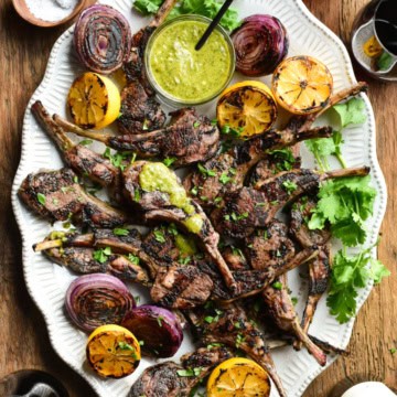 A platter of Charred Green Onion-Jalapeno-Lemon Lamb Chops with sauce, grilled onions and lemons.