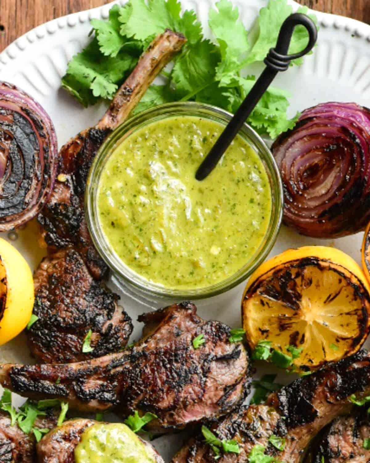 A bowl of sauce served with grilled lamb chops, onions and lemons.