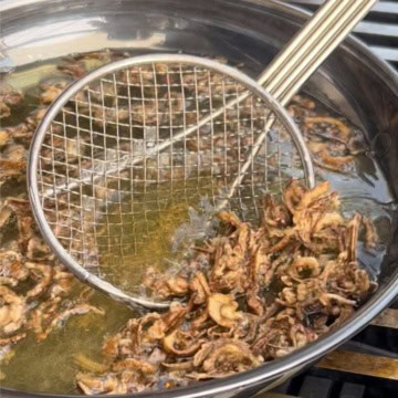 Scooping fried shallots out of a pan with oil.