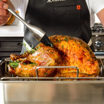 A side shot of a golden turkey getting baked in the roaster.