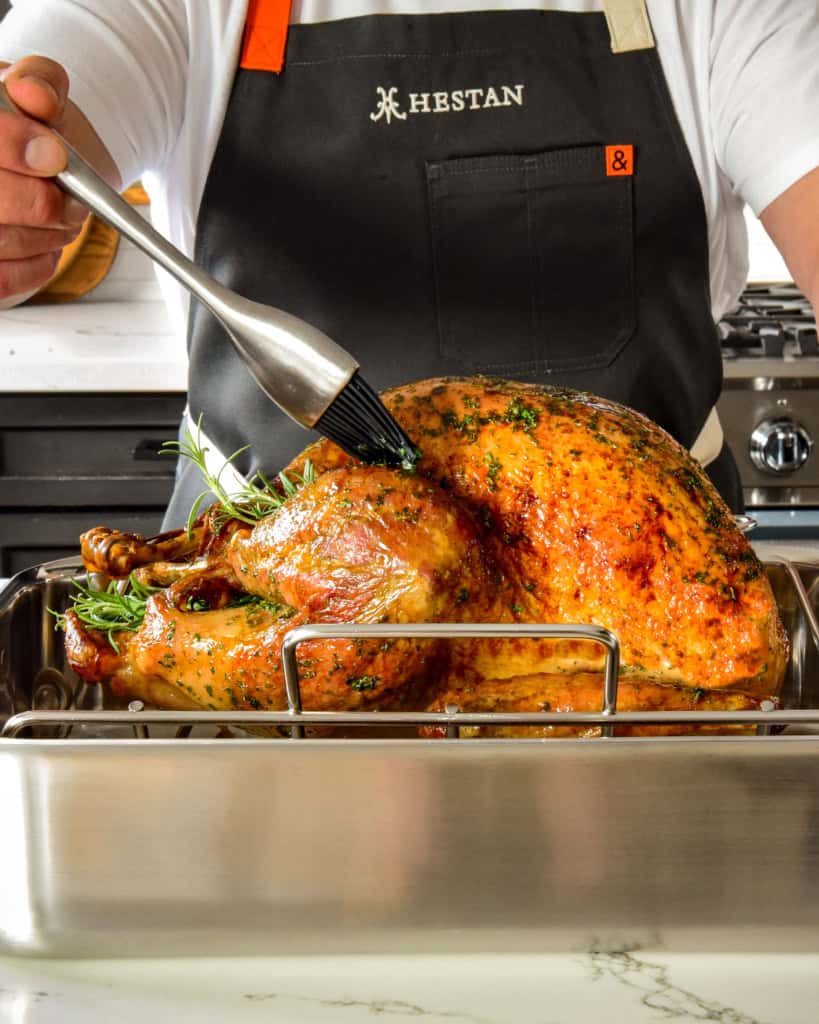 A side shot of a golden turkey getting baked in the roaster.