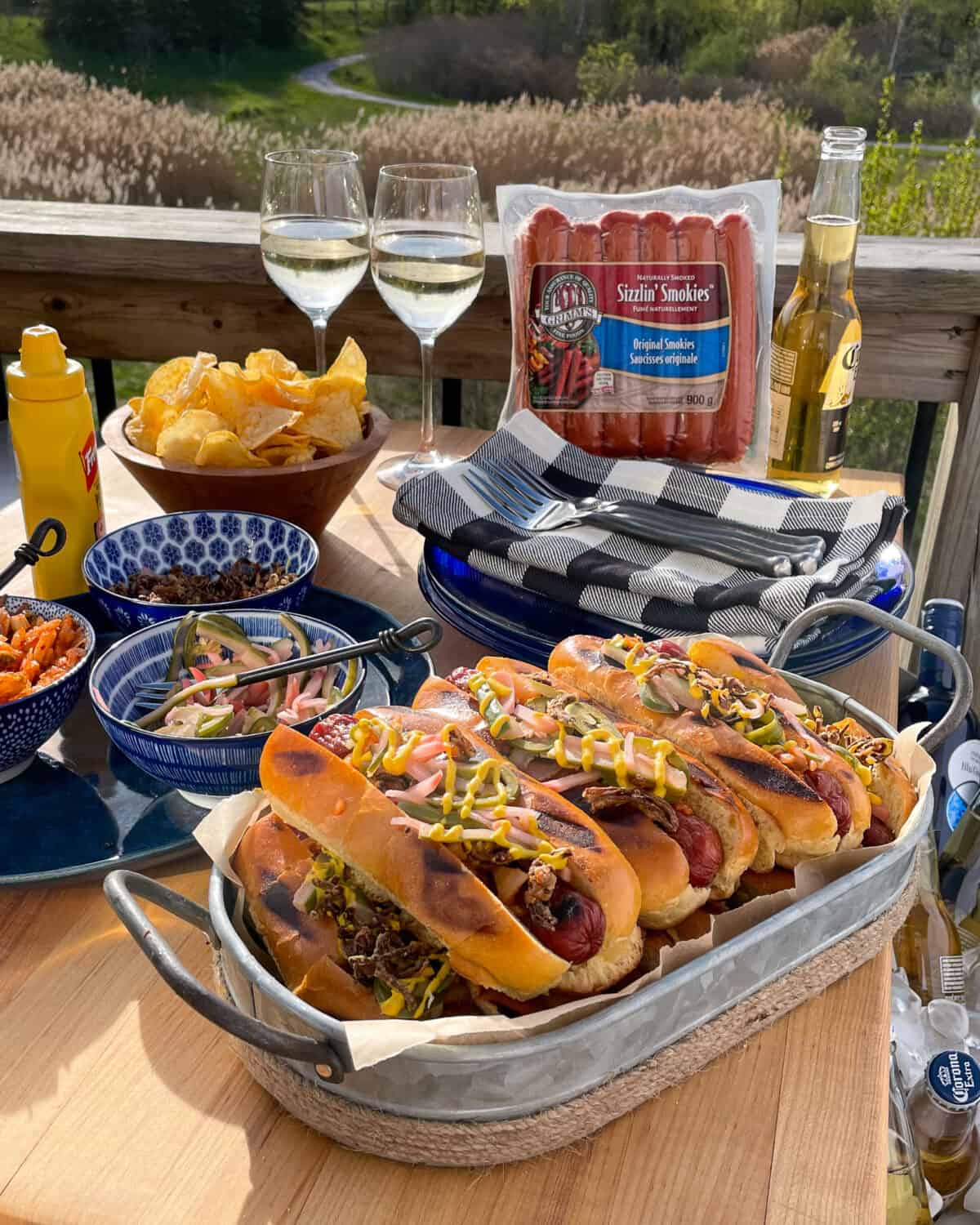 A summer spread with a tray of loaded smokies, toppings, dinnerware, wine and a pack of smokies.