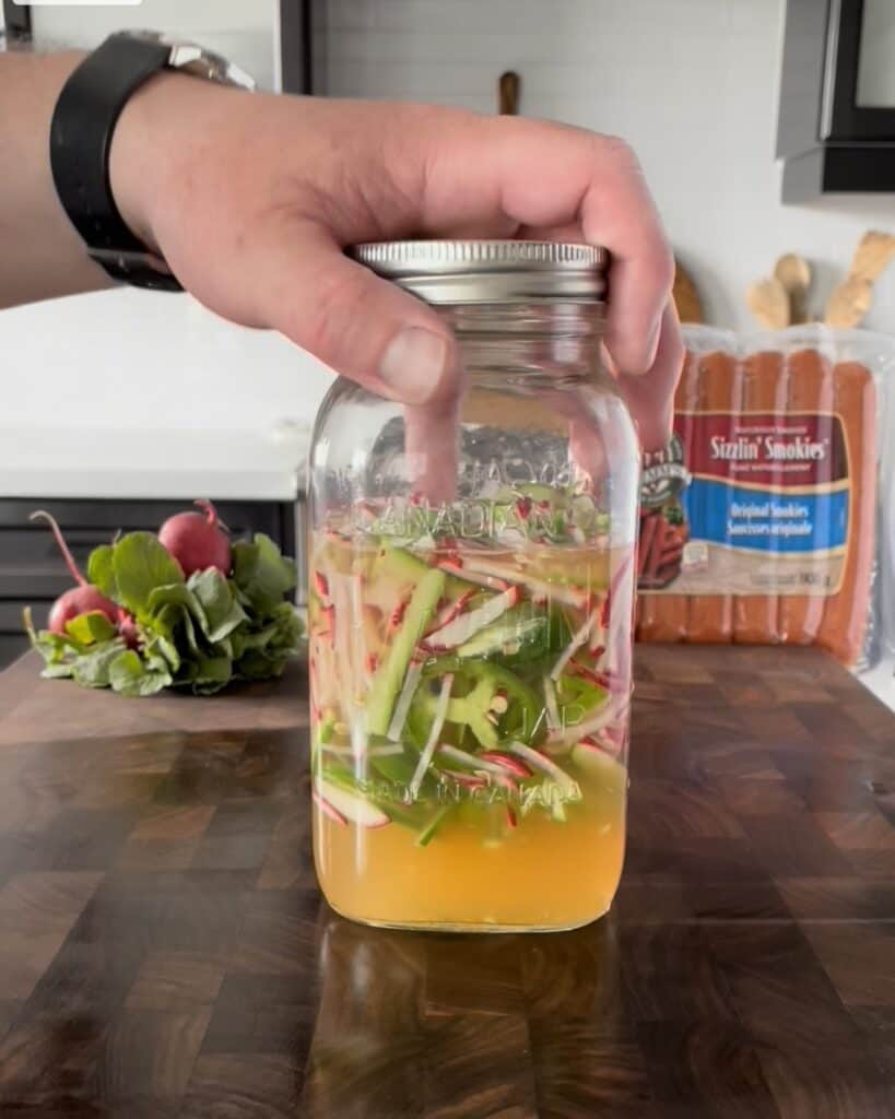 A mason jar with sliced vegetables in a pickling solution.