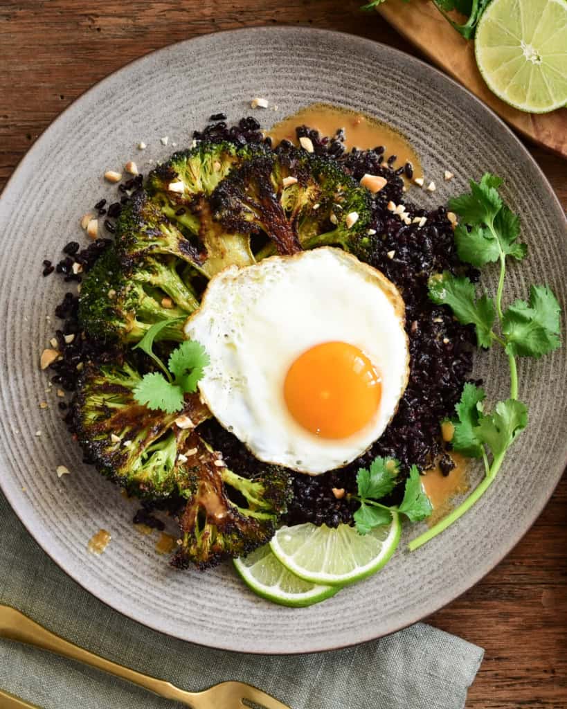 A serving of a stir-fried black rice with broccoli and a fried egg.