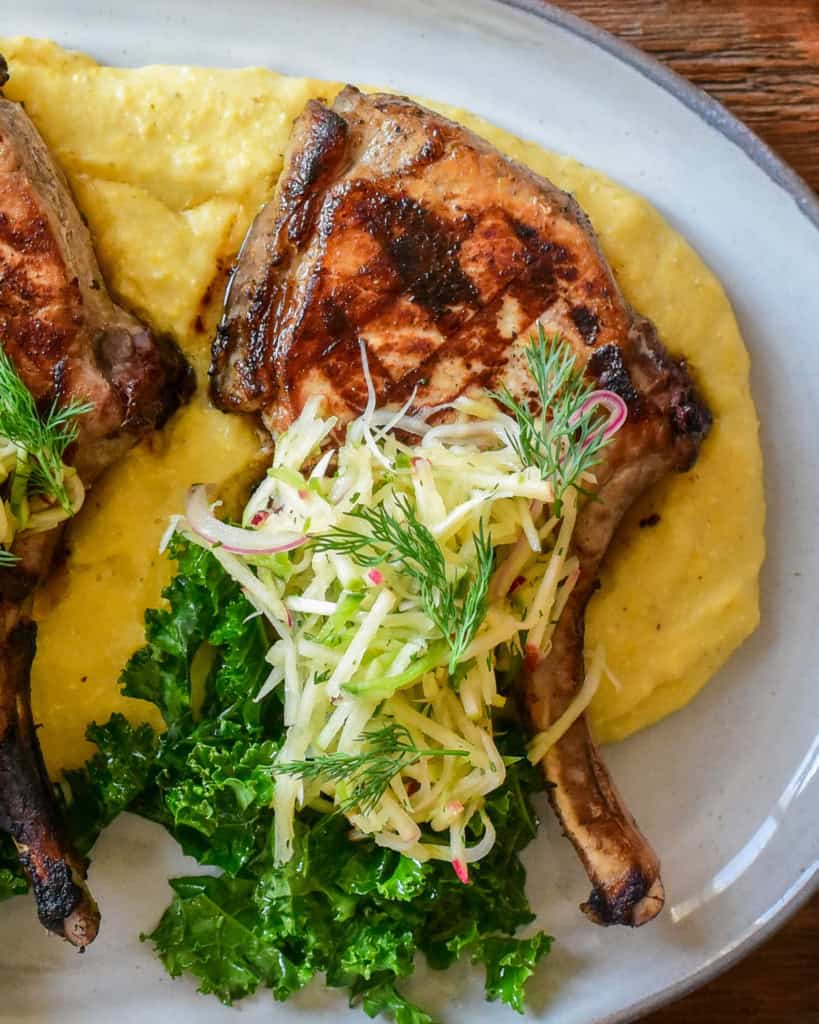 A platter of creamy polenta served with pork chops and apple slaw.