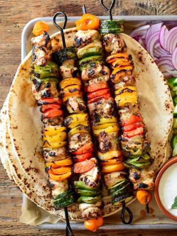 Four colourful grilled chicken and vegetable skewers served with pita.