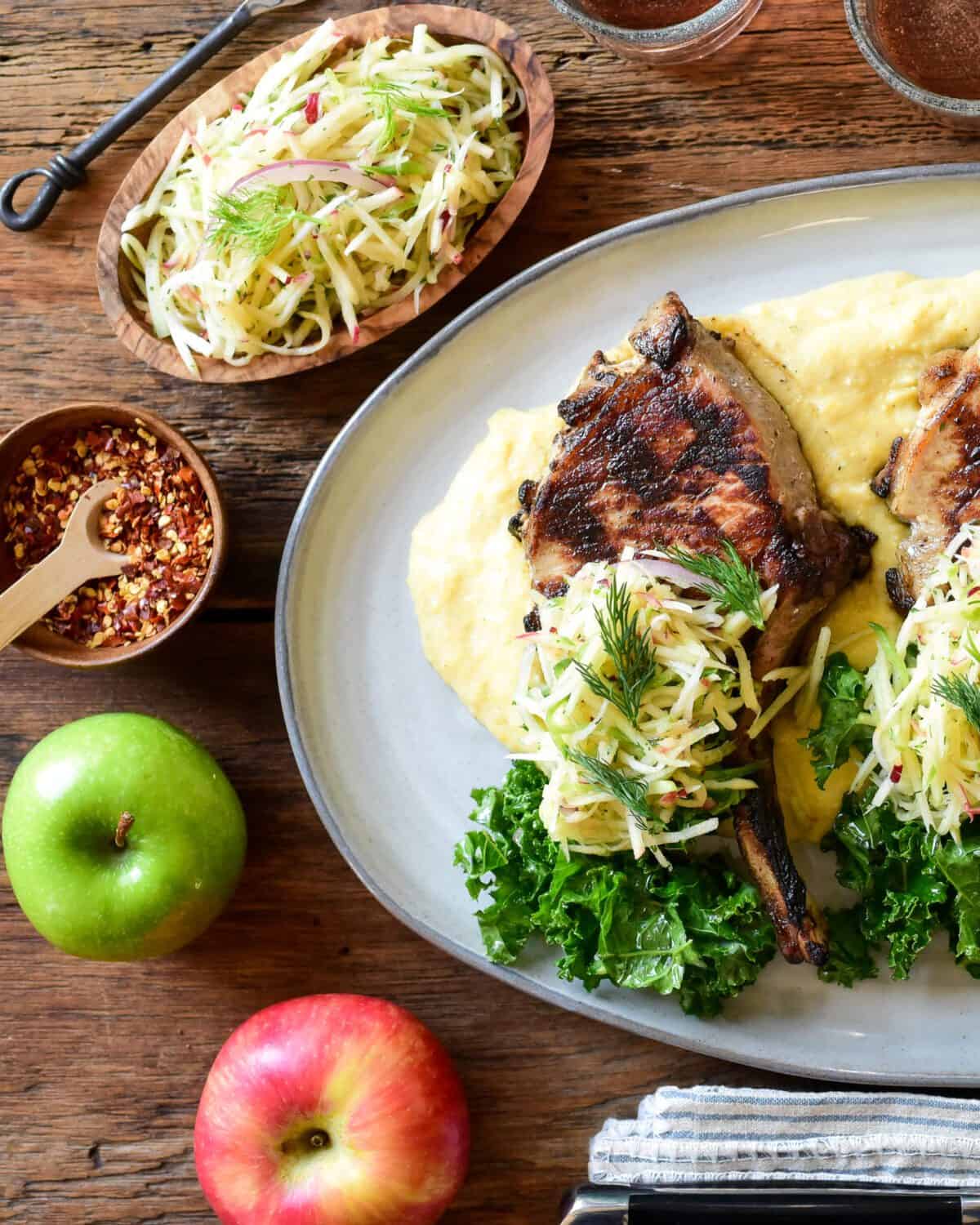 A grilled pork chop with a pile of apple slaw on a bed of polenta.