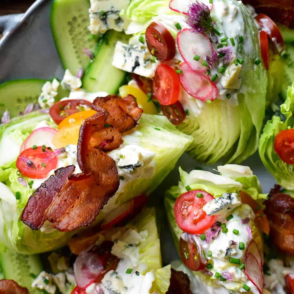 A round platter with six wedge salads topped with dressing, cheese, tomatoes and a strip of bacon. Served with rose wine.
