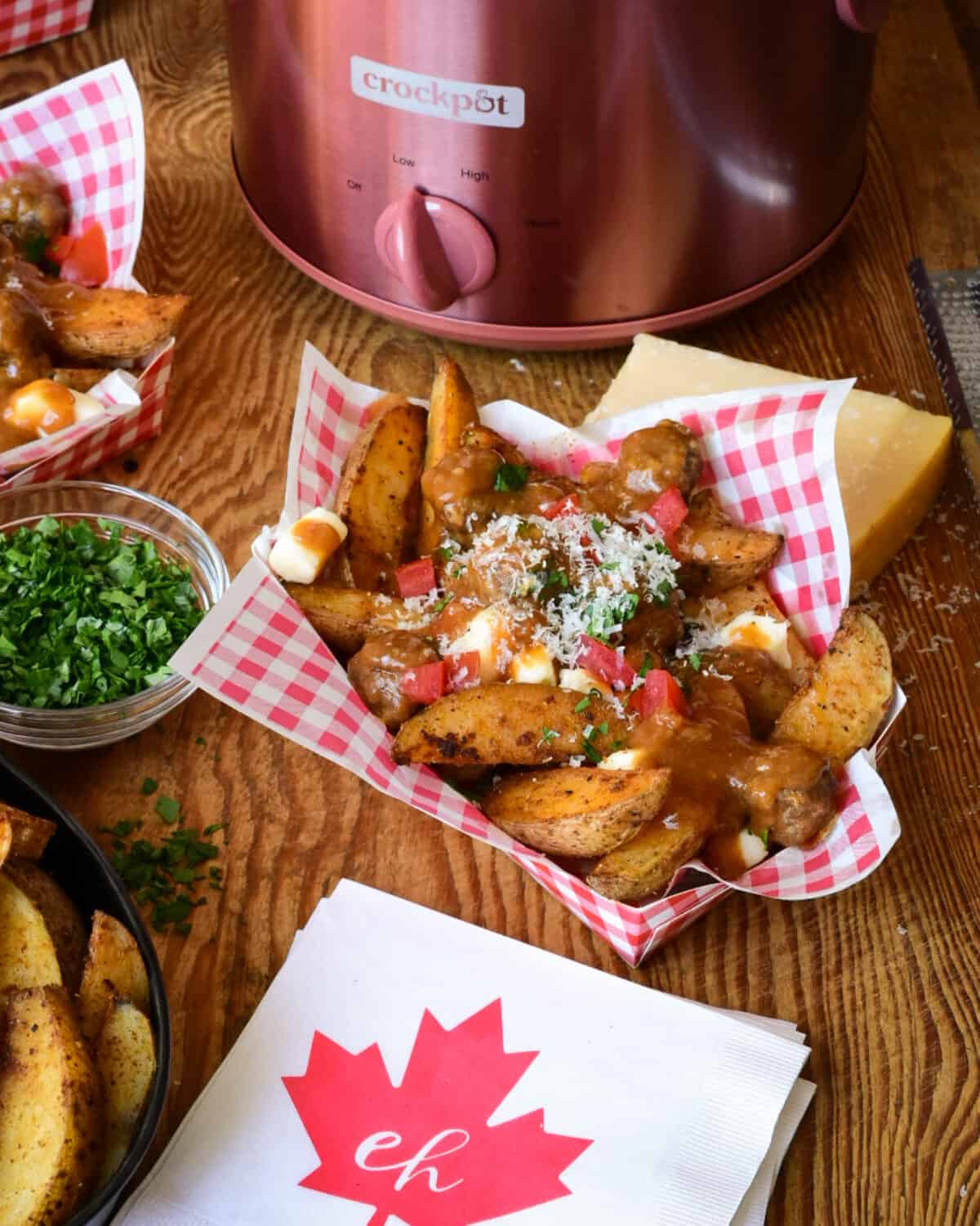 A close up view of poutine with meatballs. A red and white check snack bowl if filled with potato wedges and cheese curds which are covered in gravy and meatballs.