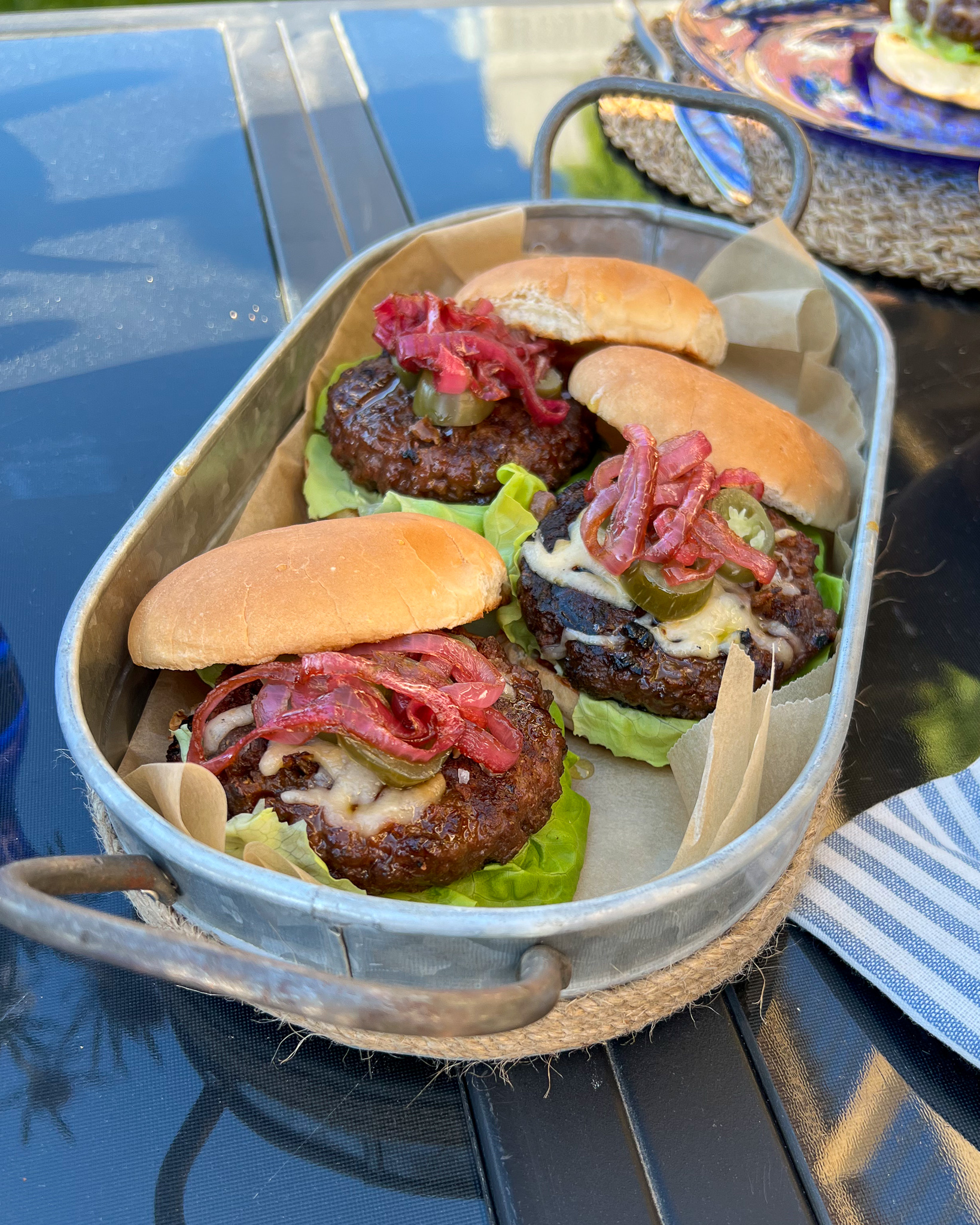 Three fully loaded burgers are in tray outdoors.