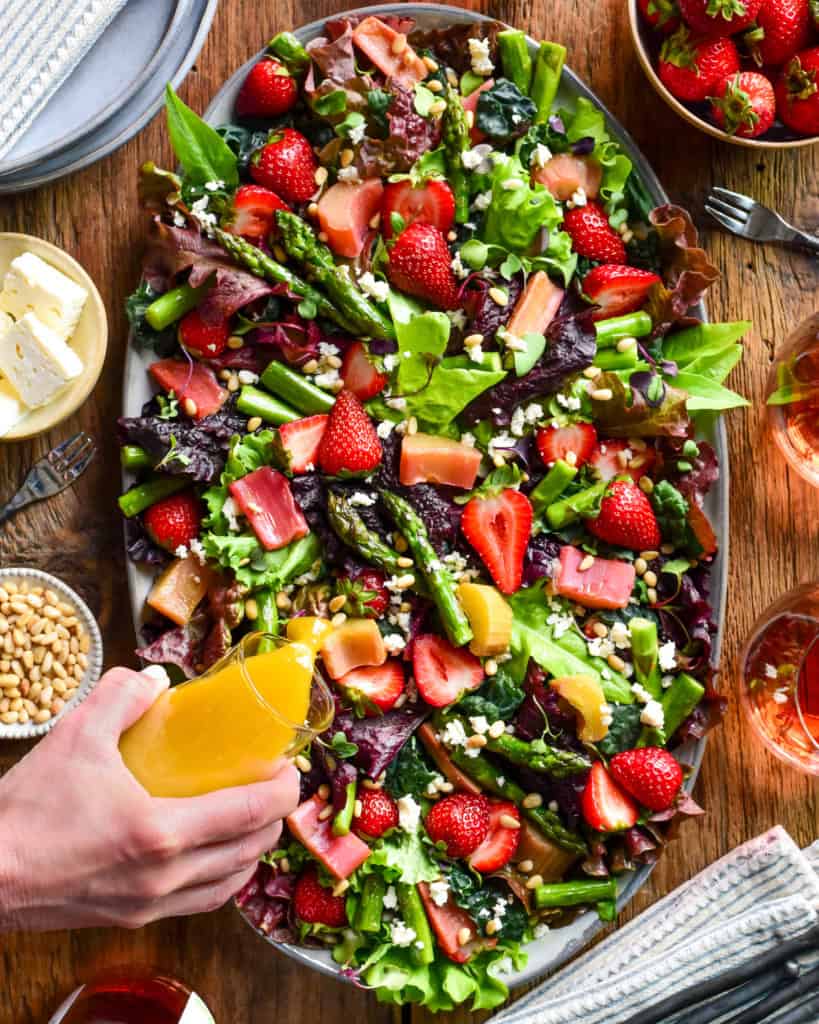 A colourful strawberry, asparagus and rhubarb salad. Dressing is getting poured over it.